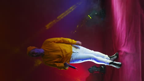 Vertical-video.-A-singer-in-a-yellow-suit-dances-and-sings-with-a-microphone-in-neon-color.-Jump-and-move-vigorously.